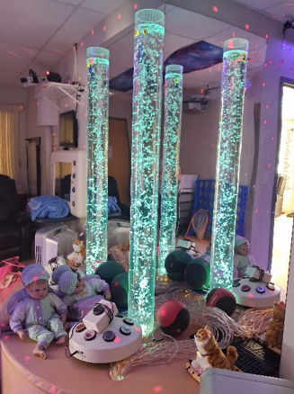 A close up of a corner in the sensory room, with a bubble towers and mirrored walls, stuff animals, dolls, balls and lights.