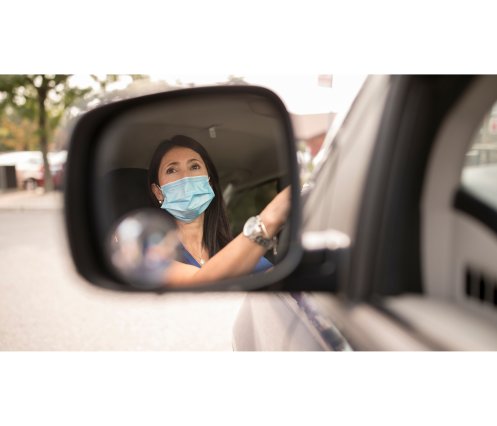 A masked individual at their wheels, photographed through their rear-view mirror