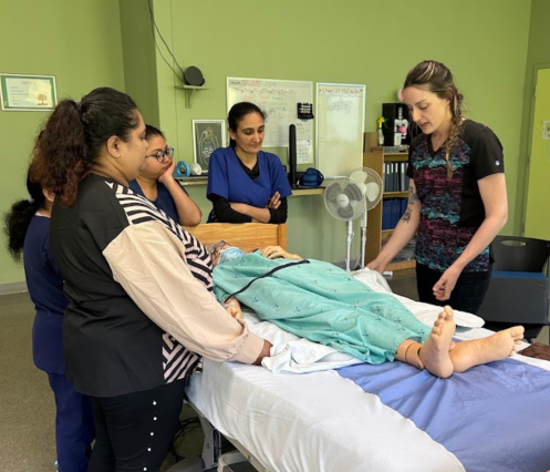 A group of students and an instructor grouped around a stretcher with a manikin