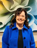 Headshot of Cindy MacQuarrie, Chief Nursing Officer wearing a cobalt blue jacket and a colourful painting in the background.